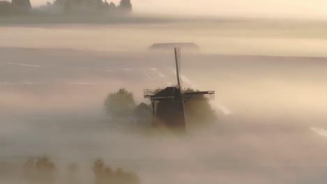 Aerial-view-of-traditional-old-windmill-in-a-meadow-with-low-fog-at-sunrise,-Friesland,-Netherlands