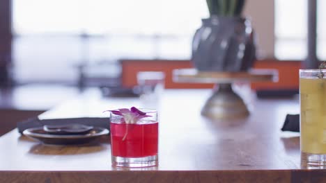 Dolly-shot-of-orange-cocktail-with-a-thyme-garnish-and-a-red-cocktail-with-a-flower-garnish-in-a-Japanese-sushi-restaurant-with-the-video-in-slow-motion