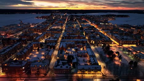 Twilight-descends-on-snowy-Luleå,-city-lights-glowing-warmly,-aerial-view