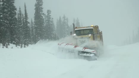 Gelber-Kanadischer-Schneepflug-LKW-Fährt-In-Zeitlupe-Auf-Die-Kamera-Zu,-Während-Er-An-Einem-Verschneiten,-Bewölkten-Tag-Die-Landstraße-Von-Frisch-Gefallenem-Schnee-Räumt