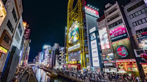 Night-time-lapse-of-Dotonbori-Canal-with-City-lights,-boats-and-crowds-outside-the-Ebisu-Tower-Ferris-Wheel-Don-Quixote-at-the-Namba-Osaka,-Japan