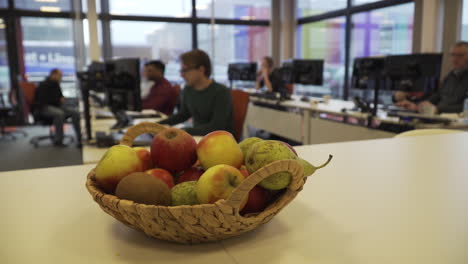 Nahaufnahme-Eines-Gesunden-Obstkorbs-In-Einem-Büro-Mit-Menschen,-Die-Im-Hintergrund-Arbeiten