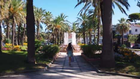 Una-Joven-Camina-Por-El-Parque-Con-Una-Fuente-En-Antibes-En-Verano,-Inclinada-Hacia-Arriba