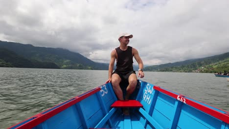 American-Tourist-Cruising-on-Wooden-Boat-on-Phewa-Lake-Sitting-on-the-Bow-and-Admire-Nature-Traveling-in-Pokhara-Nepal,-Happy-Man