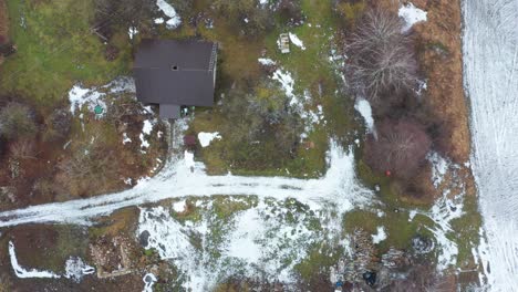 Aerial-top-down-ascend-view-over-colorful-cottage-yard,-frozen-road-and-field