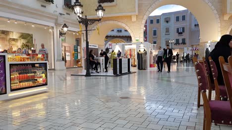 Doha,-Katar,-Villaggio-Einkaufszentrum,-Frauen-In-Traditioneller-Muslimischer-Kleidung-Und-Menschen-Zu-Fuß-Zwischen-Den-Geschäften