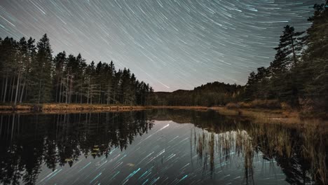 Sternenhimmel-Mit-Sternspuren,-Die-Sich-In-Einem-Zeitraffervideo-In-Der-Ruhigen-Oberfläche-Des-Dunklen-Sees-Spiegeln