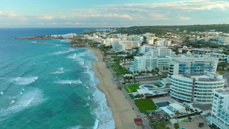 Vista-Aérea-De-Protaras,-Una-Ciudad-Turística-En-Chipre,-Que-Muestra-Su-Playa-De-Arena-Bordeada-De-Hoteles-Y-Complejos-Turísticos,-Su-Vibrante-Vegetación-Y-Las-Atractivas-Aguas-Turquesas-Del-Mar-Mediterráneo.