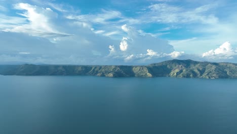 Expansive-view-of-Lake-Toba-with-surrounding-mountains-under-a-blue-sky,-Sumatra,-Indonesia,-aerial-shot