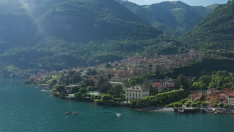 Lush-greenery-surrounds-Lake-Como-in-Ossuccio,-Italy,-boats-gently-drift,-mountain-backdrop