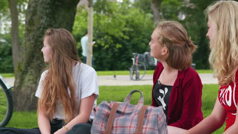Three-young-girls-outside-looking-over-their-shoulders-in-a-green-park,-slowmo