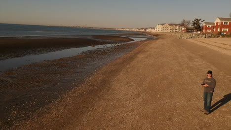 Drone-flying-fast-backwards-across-a-beach-with-a-person-in-the-distance