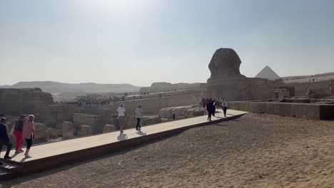 Tourists-walk-by-the-Sphinx-and-Pyramids-in-Egypt,-under-a-clear-sky