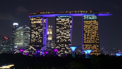 Night-time-lapse-shot-capturing-Singapore-city-skyline,-modern-architecture-of-Marina-bay-sands,-a-5-star-integrated-resort-hotel-with-vivid-lights-and-light-up-Supertree-grove-at-Gardens-by-the-bay