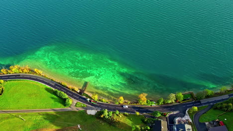 Cars-driving-on-road-winding-along-green-shore-of-beautiful-lake