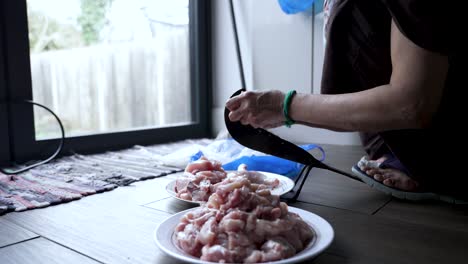 Woman-using-traditional-aruvamanai-to-cut-chicken-indoors,-natural-light,-close-up