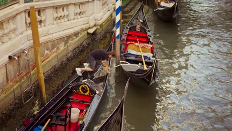 Young-man-cleaning-and-taking-care-of-his-"Gondola",-typical-boat-of-Venice,-on-a-water-canal