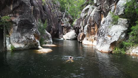 A-women-tourist-swims-through-a-water-filled-gorge-surrounded-by-towering-walls-of-Australian-sandstone