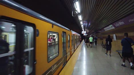 Yellow-Train-departs-from-Buenos-Aires-City-Underground-Subway-Station-People-commute-at-daily-transportation-in-Argentina,-Emilio-Mitre-in-Caballito