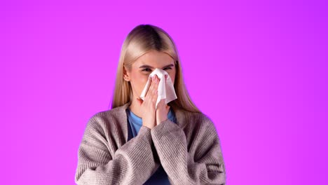 European-blonde-woman-blows-her-nose-with-a-tissue-paper,-portrait-shot-in-studio-with-infinite-magenta-background