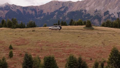Aerial-sideview-of-SUV-driving-between-grassy-dirt-road-in-mountains,-pan-to-track-and-follow