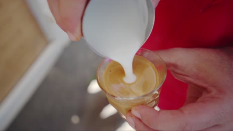 Barista-performing-latte-art-on-top-of-the-coffee-using-milk,-handheld-closeup