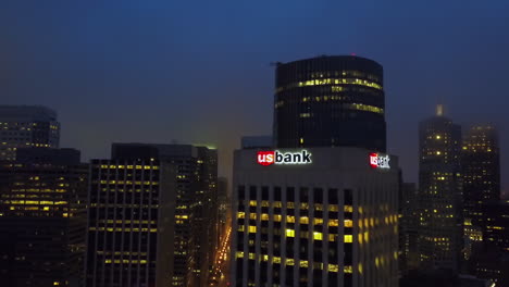 Drone-Inclinándose-Hacia-La-Noche-Nos-Iluminó-La-Torre-Del-Banco,-En-La-Sombría-San-Francisco,-Estados-Unidos