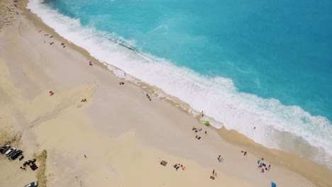 Myrtos-Strand-Mit-Türkisfarbenem-Wasser-Und-Vereinzelten-Sonnenanbetern-Auf-Sand,-Kefalonia,-Griechenland,-Luftaufnahme