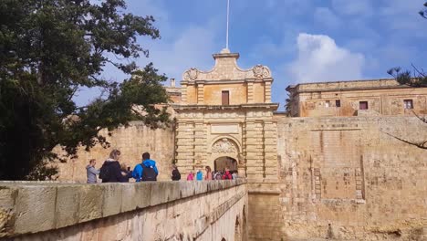 Tourists-on-the-bridge-leading-to-the-entrance-of-the-fortified-city-Mdina,-Malta