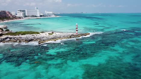 Cancun-coastline-with-a-lighthouse-on-a-sunny-day,-clear-turquoise-waters,-aerial-view