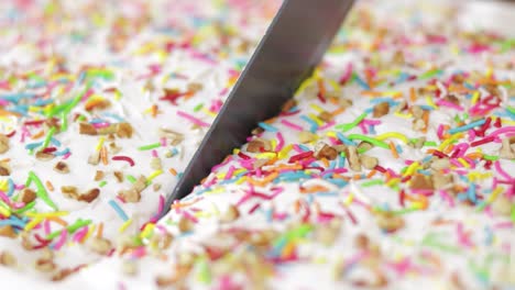 Slicing-with-knife-a-cake-covered-with-frosting,-sprinkles-and-chopped-nuts