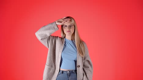 Ill-young-woman-checks-for-fever-and-sneezes-in-napkin,-red-background