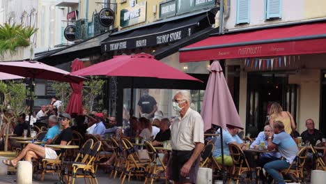 People-in-face-masks-move-by-outdoor-restaurants-in-Antibes,-France