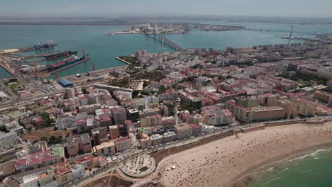 aerial-drone-forward-and-tilt-up-shot-of-Cadiz-city-with-view-of-Puente-de-la-Constitucion,-harbor-coastal-zone,-Cadiz-Spain
