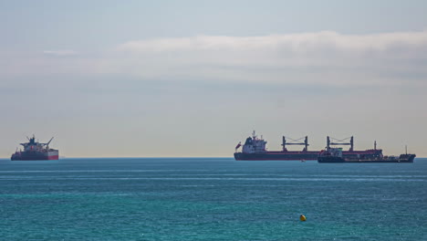 Huge-industrial-cargo-ships-on-sea,-small-boats-passing-by,-timelapse