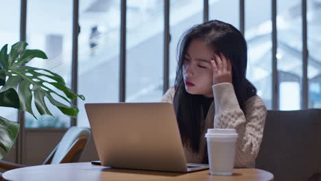 Young-Asian-girl-in-bad-mood-working-online-on-her-laptop-from-cafe