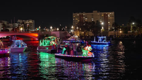 Festive-snowman-inflatable-and-flashing-string-lights-on-pontoon-boats-parade-up-and-down-canal-at-night