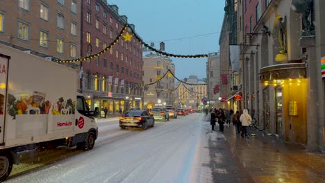 Noche-Nevada-Con-Luces-Navideñas-En-Kungsgatan-De-Estocolmo,-Llena-De-Peatones-Y-Tráfico