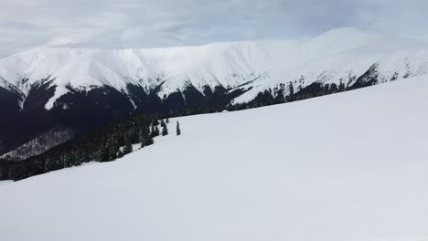 Skiers-in-line-ascending-snowy-Papusa-Peak-under-cloudy-skies,-Romania