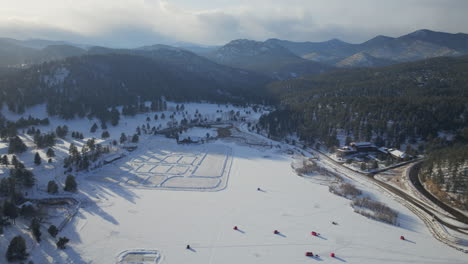 Sunset-Ice-skating-skate-hockey-rink-lake-pond-hockey-winter-Etown-Evergreen-Lake-house-fishing-tents-Denver-golf-course-Colorado-aerial-cinematic-drone-golden-hour-winter-snow-traffic-slow-backward
