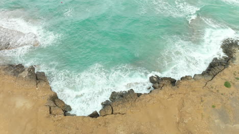 Turquoise-sea-waves-crash-over-rocky-cracked-eroded-deserted-coastline-making-foam-Cyprus---Aerial-drone-top-down-tilt-reveal-view