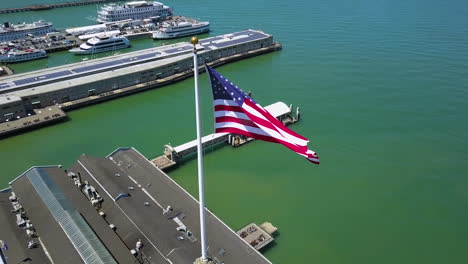 Aerial-view-away-from-a-US-flag-on-the-Ferry-Building-tower,-in-Embarcadero,-San-Francisco