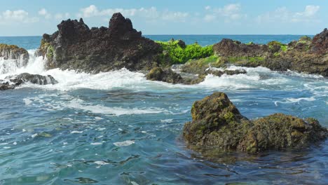 Splashes-of-water-towards-the-rocks-covered-in-algae-on-the-seashore,-static-closeup-slow-motion-low-angle