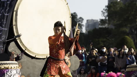 Hombre-Con-Traje-Tradicional-Tocando-Tambores-En-Una-Danza-Del-Dragón-Chino-En-Taipei,-Observando-Multitudes,-Luz-Del-Día,-Ambiente-Festivo,-Vista-Lateral