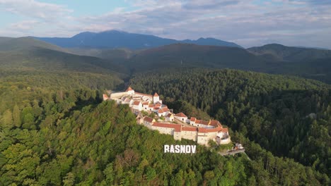 Castillo-De-La-Fortaleza-De-Rasnov-En-La-Cima-De-Una-Colina-En-Los-Cárpatos,-Rumania---Círculos-Aéreos-4k