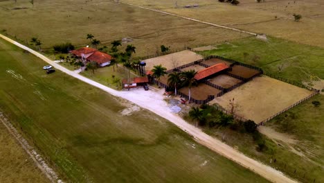 Drone-flight-over-farm,-with-its-large-field,-stables-and-fences