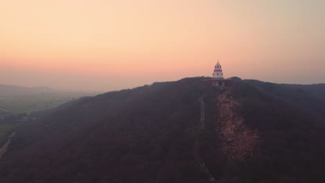 Toma-Aérea-De-Un-Templo-Hindú-En-La-Cima-De-Una-Colina-Con-Escaleras-Que-Conducen-A-él-Durante-La-Puesta-De-Sol-En-Un-Pueblo-De-Gwalior-En-Madhya-Pradesh,-India