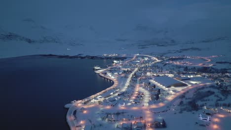 Cozy-snowy-illuminated-village-during-winter,-Icelandic-fjord-by-night