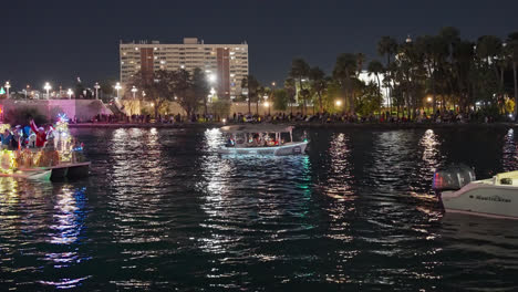 Gente-Disfrazada-De-Papá-Noel-Parada-En-Un-Barco-Iluminado-Por-La-Noche-Y-Saludando