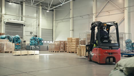 Cámara-Lenta-De-Un-Trabajador-De-Almacén-Operando-Un-Montacargas-Rojo-Con-Carga-Dentro-De-Un-Nuevo-Almacén-Lleno-De-Cajas-En-El-Hangar-Del-Aeropuerto